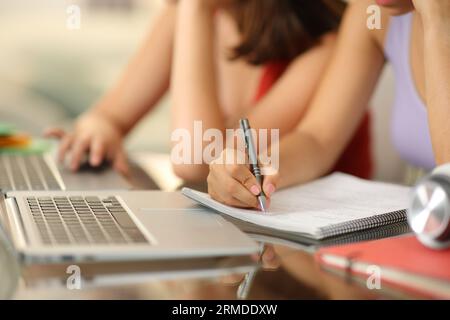 Gros plan portrait de deux mains d'élèves à l'aide d'un ordinateur portable et en prenant des notes Banque D'Images