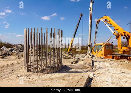 Partie supérieure, barres d'armature, de renfort de pilier de béton dans la base. Grue mobile et pompe de camion versant du béton frais dans la fondation de pont en b. Banque D'Images