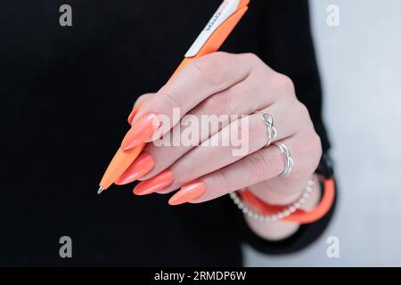 main féminine tenant un stylo orange sur un fond noir Banque D'Images