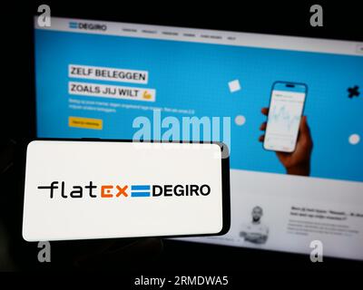 Personne tenant le téléphone portable avec le logo de la société Fintech allemande Flatexdegiro AG sur l'écran en face de la page Web d'affaires. Concentrez-vous sur l'affichage du téléphone. Banque D'Images