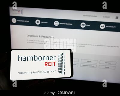 Personne tenant le téléphone portable avec le logo de la société immobilière allemande Hamborner Reit AG sur l'écran en face de la page Web. Concentrez-vous sur l'affichage du téléphone. Banque D'Images