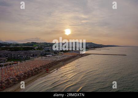 Une vue aérienne d'une plage au coucher du soleil avec un éventail de parasols colorés sur le rivage Banque D'Images