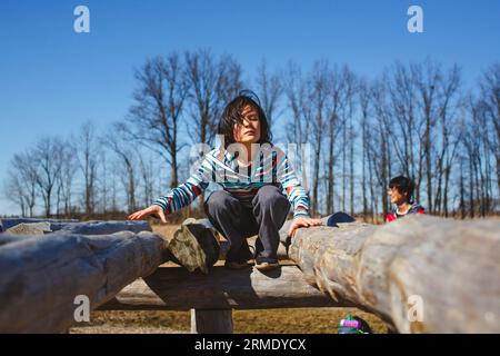 Un enfant se perche sur la structure en bois dans le parc avec le père en arrière-plan Banque D'Images