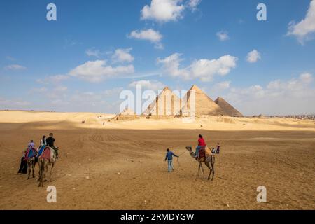 Touristes explorant les grandes pyramides de Gizeh à chameaux Banque D'Images