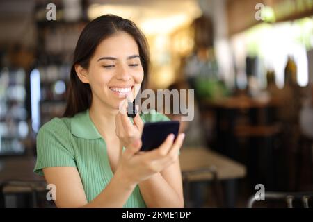 Femme heureuse peignant des lèvres assis dans un restaurant attendant dans une date Banque D'Images