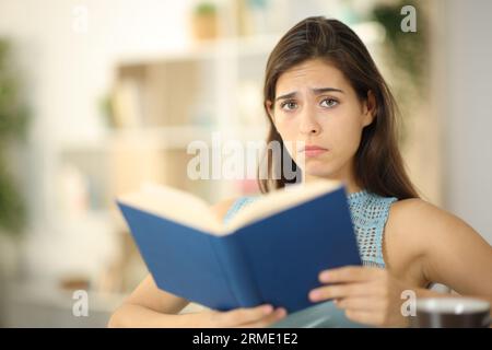 Triste lecteur de livres regardant la caméra assis à la maison Banque D'Images