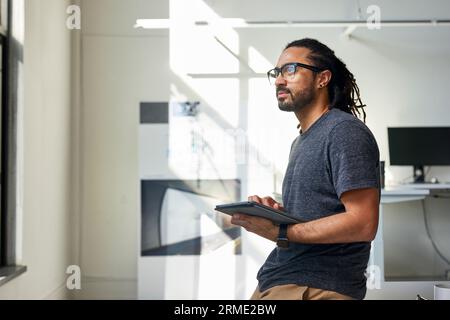 Vue de côté de l'homme d'affaires réfléchi avec tablette debout contre le mur dans le bureau Banque D'Images