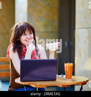 Belle jeune fille travaillant ou étudiant dans un café et buvant une boisson chaude Banque D'Images