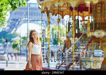 Belle jeune femme parisienne en jupe longue près de la tour Eiffel et manège traditionnel français un jour d'été Banque D'Images