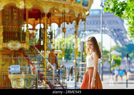 Belle jeune femme parisienne en jupe longue près de la tour Eiffel et manège traditionnel français un jour d'été Banque D'Images