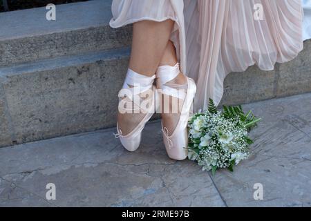 Ballerine femelle. Jambes de jeune belle danseuse de ballet femme, habillée en tenue professionnelle, chaussures pointe sur fond urbain, gros plan. Banque D'Images