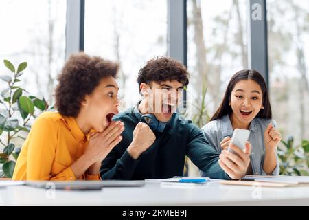 Des partenaires émotionnels divers regardant le téléphone portable, serrant les poings et criant oui, vérifiant les résultats des examens en ligne Banque D'Images