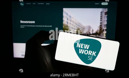 Personne tenant le téléphone portable avec le logo de la société allemande New Work se (XING) sur l'écran en face de la page Web de l'entreprise. Concentrez-vous sur l'affichage du téléphone. Banque D'Images