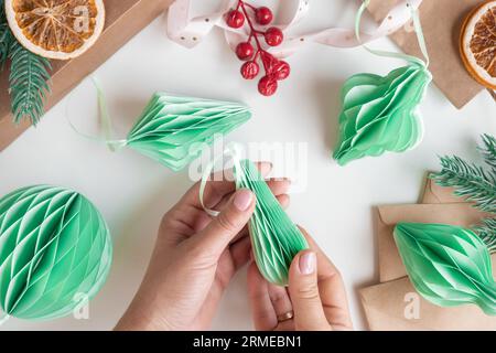 Les mains féminines déplient des ornements en nid d'abeille de Noël en papier. Décoration sans plastique pliable faite à la main. Concept d'artisanat de créativité hivernale. Mode éco DIY. SC Banque D'Images