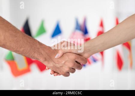 Dame européenne millénaire serrant la main à l'homme dans l'intérieur du bureau avec de nombreux drapeaux différents, floutés, recadrés Banque D'Images