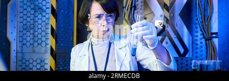 femme scientifique d'âge moyen dans des lunettes regardant le liquide dans le tube à essai dans le laboratoire d'innovation, bannière Banque D'Images