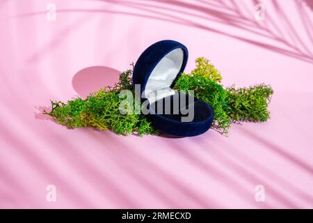 Boîte à bijoux vide sur mousse de lichen stabilisée et fond rose avec des ombres de feuilles de palmier, fond minimal pour le placement de produit Banque D'Images