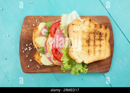 tranches de pain grillées avec concombre, oignon, tomates, laitue et salami, sandwich sur une planche à découper en bois, texture plate Banque D'Images