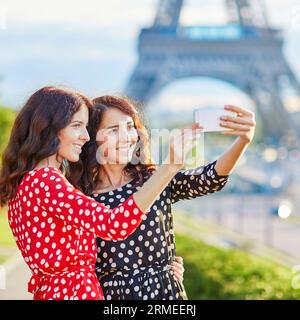 Sœurs jumelles prenant un selfie près de la tour Eiffel à Paris. Touristes profitant de leurs vacances en France. Date romantique ou concept de couple voyageur Banque D'Images