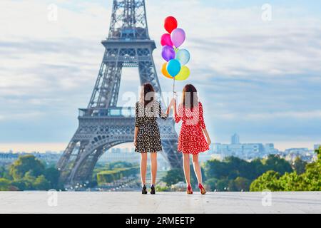 Belles sœurs jumelles dans des robes à pois rouges et noires avec un énorme bouquet de ballons colorés devant la tour Eiffel à Paris, France Banque D'Images
