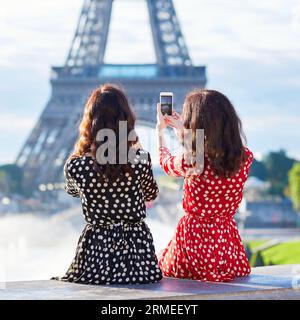 Sœurs jumelles prenant un selfie près de la tour Eiffel à Paris. Touristes profitant de leurs vacances en France. Date romantique ou concept de couple voyageur Banque D'Images