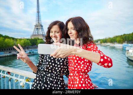 Belles sœurs jumelles prenant selfie devant la Tour Eiffel lors d'un voyage à Paris, France. Les filles souriantes heureuses apprécient leurs vacances en Europe Banque D'Images