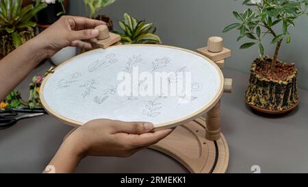 La main d'une femme tient un cerceau en bois pour commencer à coudre des fleurs à broder. Banque D'Images