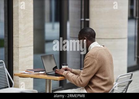 Jeune homme afro-américain cols blancs regardant l'écran d'ordinateur portable et tapant sur le clavier tout en travaillant sur un nouveau projet d'entreprise Banque D'Images
