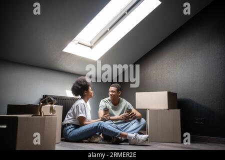 joyeux couple afro-américain avec du café pour aller parler près des boîtes en carton sur le grenier dans la nouvelle maison Banque D'Images