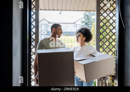 couple afro-américain romantique souriant tenant des boîtes en carton près de la porte de la nouvelle maison Banque D'Images