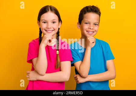 Photo de jolies écoliers préadolescents habillés t-shirts souriants mains bras mentons isolé fond de couleur jaune Banque D'Images