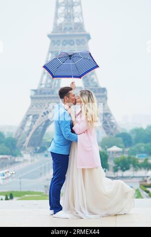Juste un couple marié sous parapluie par temps de pluie près de la tour Eiffel le jour de leur mariage. Mariée et marié à Paris, France Banque D'Images