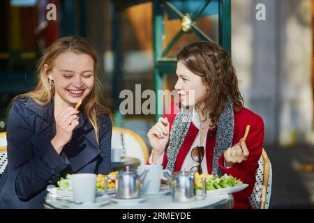 Deux jeunes filles dans un café parisien en plein air, mangeant des frites. Concept d'amitié Banque D'Images