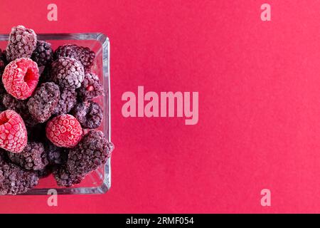 Micro gros plan de framboises dans un bol en verre avec espace de copie sur fond rouge Banque D'Images
