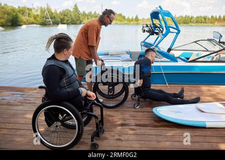 Portrait vue de côté de deux personnes handicapées utilisant de l'équipement sportif adaptatif sur la jetée du lac, espace de copie Banque D'Images