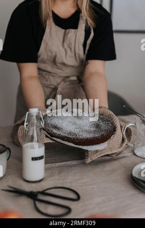 Femme mettant un gâteau au chocolat fraîchement cuit sur la table Banque D'Images