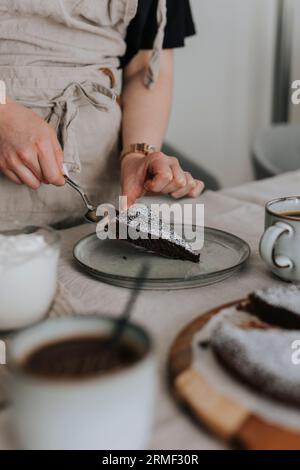 Femme mettant morceau de gâteau au chocolat fraîchement cuit sur l'assiette Banque D'Images