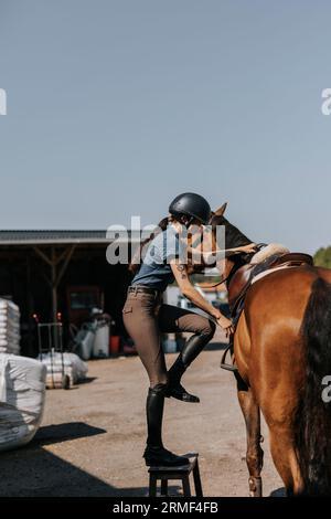 Vue latérale de la femme montant à cheval au paddock Banque D'Images