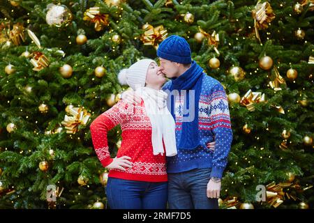 Couple heureux dans des pulls colorés près du bel arbre de Noël avec des boules d'or Banque D'Images