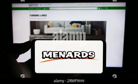 Personne détenant un téléphone cellulaire avec le logo de la société de détail américaine Menard Inc. (Menards) à l'écran devant la page Web de l'entreprise. Concentrez-vous sur l'affichage du téléphone. Banque D'Images