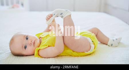 Adorable petite fille enlevant la chaussette de son pied. Petit enfant s'amusant. Enfant en bas âge dans la crèche ensoleillée Banque D'Images