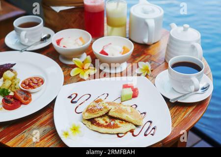 Petit-déjeuner balinais traditionnel avec nouilles frites (mie goreng), crêpe à la banane et fruits frais servis près de la piscine Banque D'Images