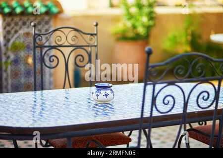 Table avec cendrier en céramique bleue et chaises jaunes dans un restaurant marocain confortable à Essaouira, Maroc Banque D'Images