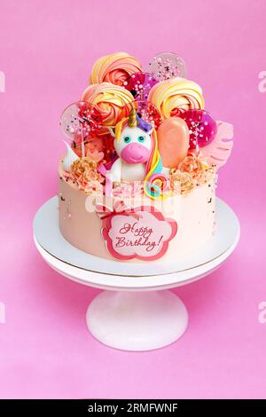 Gâteau d'anniversaire rose avec licorne fondante mignonne, sucettes, popsicles et texte Joyeux anniversaire sur un papier comestible Banque D'Images