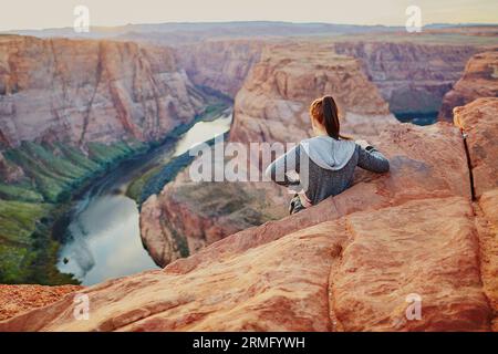 Jeune femme debout sur le bord du précipice et profitant de la vue à Horseshoe Bend, coucher de soleil dans le Colorado Canyon, Arizona, États-Unis Banque D'Images