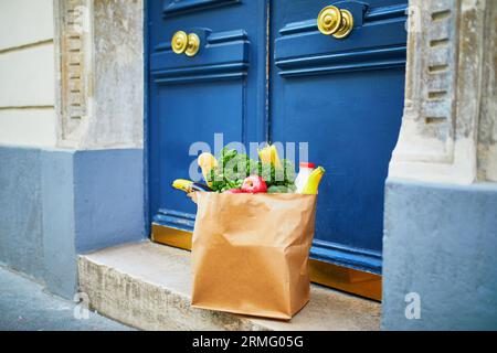 Livraison de nourriture pendant l'épidémie de coronavirus. Sac en papier avec commande d'épicerie devant la porte à Paris, France pendant l'épidémie de Covid-19. Sécurité en ligne sh Banque D'Images