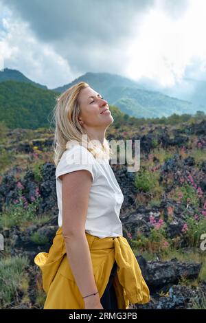 Randonnée sur le plus haut volcan d'Europe continentale - Etna. Jeune femme souriante profitant de l'air sur la pente couvert de végétation verte sur sable noir lave-roche Banque D'Images