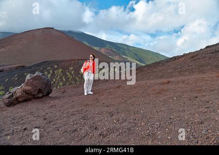 Randonnée sur le plus haut volcan d'Europe continentale - Etna. Jeune femme souriante profitant de l'air sur la pente couvert de végétation verte sur sable noir lave-roche Banque D'Images