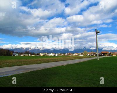 Vue du village près de Kranj à Sorsko polje dans la région de Gorenjska en Slovénie avec Kamnik-Savinja alpes dans le dos enveloppé dans les nuages et les maisons en f Banque D'Images