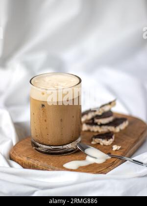 Un gros plan d'un café latte froid fraîchement préparé servi dans un verre sur une planche de bois, posé sur un drap de lit blanc Banque D'Images